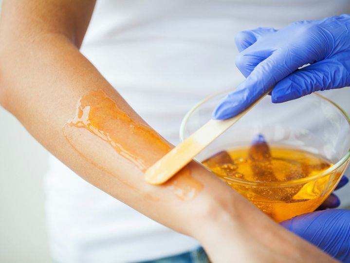 Women hold orange paraffin wax bowl. Woman in beauty salon