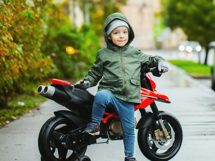 A beautiful little boy posing at his children's red motorcycle.