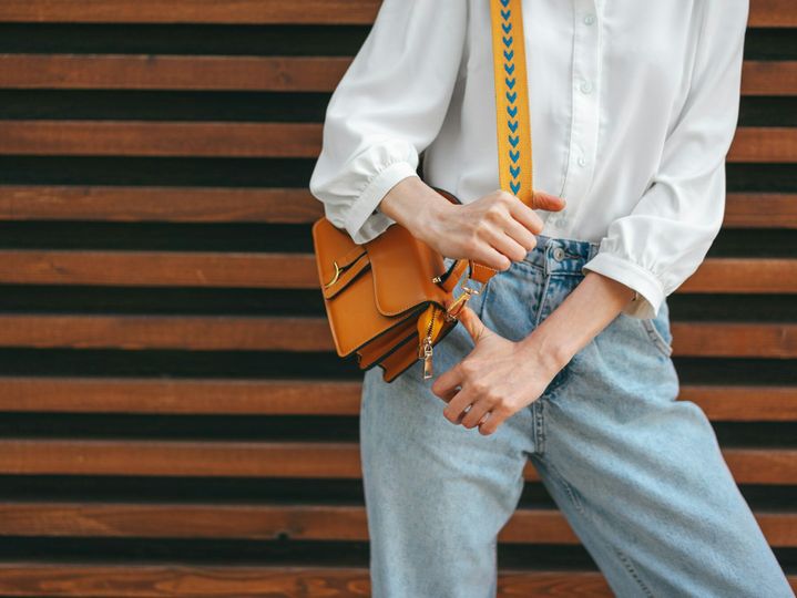 Fashion photo of woman wearing white shirt, jeans and brown crossbody bag against wooden background