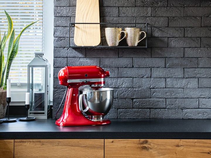 Wooden clock on black brick wall in trendy kitchen with red kitchen robot