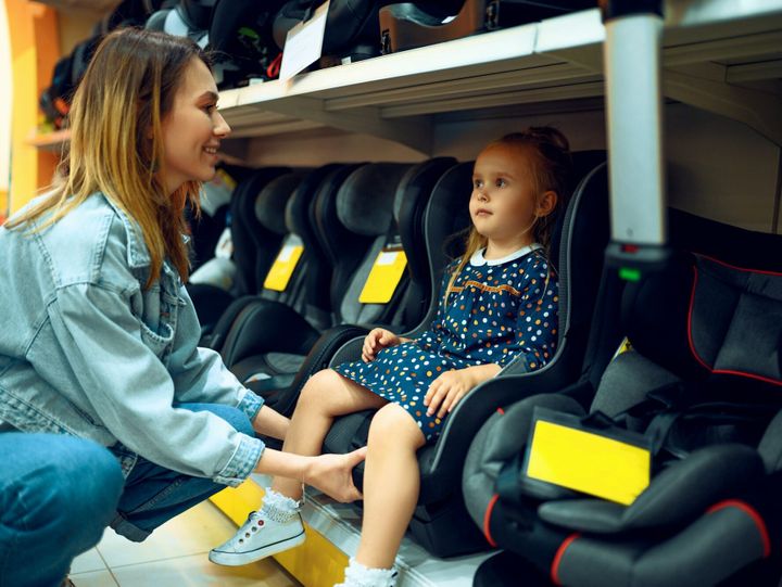 Mother and little girl choosing baby seat in store