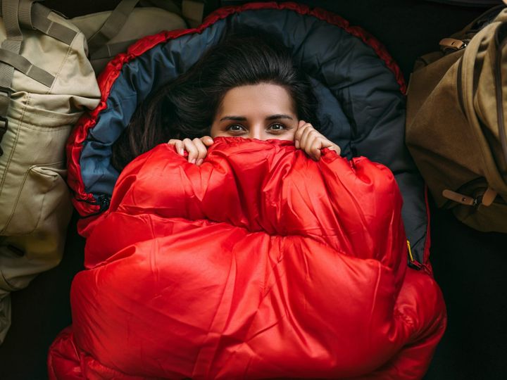 A young woman in a comfortable sleeping bag in a tent, top view. A tourist in a sleeping bag