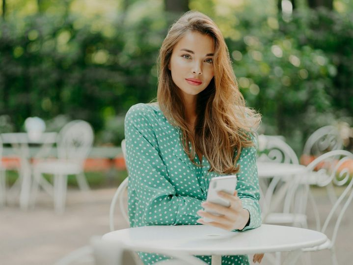 Outdoor shot of fashionable woman with long hair, dressed in green polkadot shirt