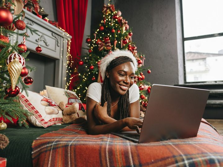 Young African woman on bed using laptop on Christmas eve