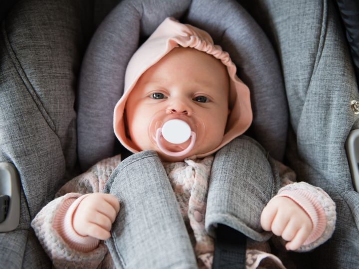 Newborn baby lies in a car seat with a pacifier
