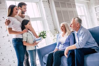 The happy girl with parents giving a gift with flowers to grandparents.