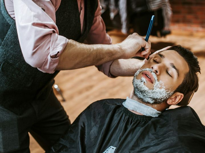 barber shaving handsome man with shaving cream on face