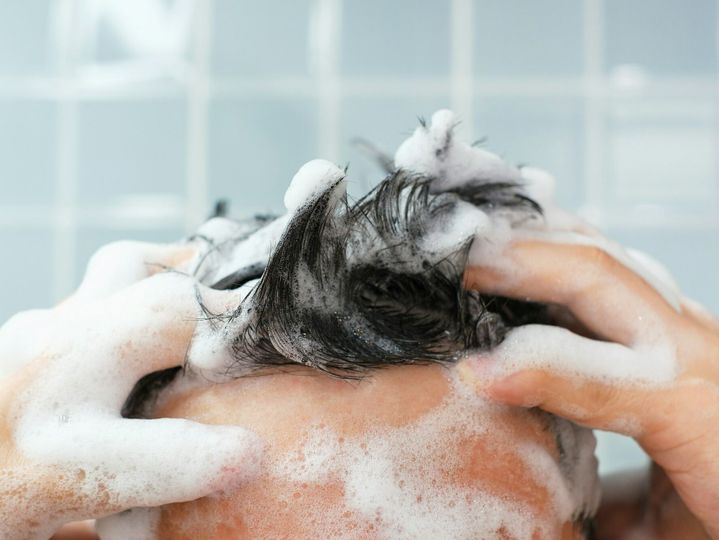 Male hands wash their hair with shampoo and foam on blue background, front view.