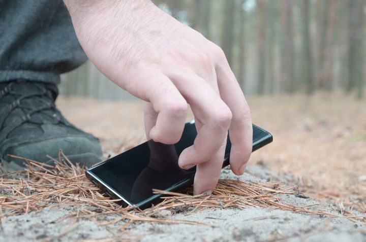 Male hand picking up lost mobile phone from a ground in autumn f