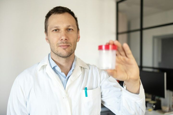 Drug test. Doctor in white uniform holding a container for semen analysis. Donor sperm for artificia