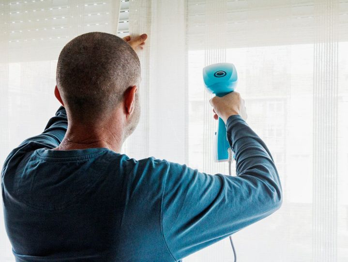 Man irons the curtains with a vertical steam iron in the living room at home, housework, ironing