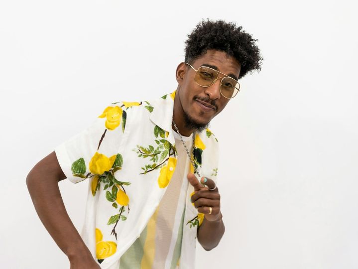 Young Afro-American male in a floral shirt and sunglasses smiling and dancing on a white background