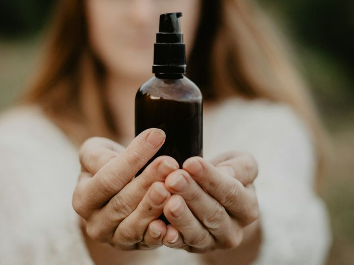 Female hands holding a dark unmarked bottle, cosmetics, natural remedies.