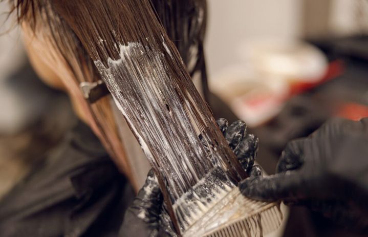 Close up of colorist dyes hair of woman with brush and foil in beauty salon