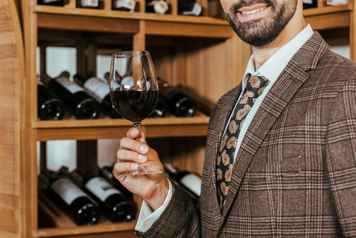 cropped shot of smiling man in tweed jacket with glass of wine at wine store