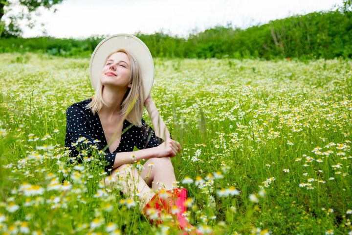 Blonde woman in black dress sitting in countryside chamomiles flowers field