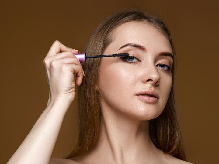 young woman applying black mascara on long thick eyelashes