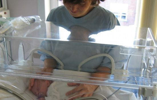 Mama wcześniaka dotyka w inkubatorze swoje nowo narodzone dz