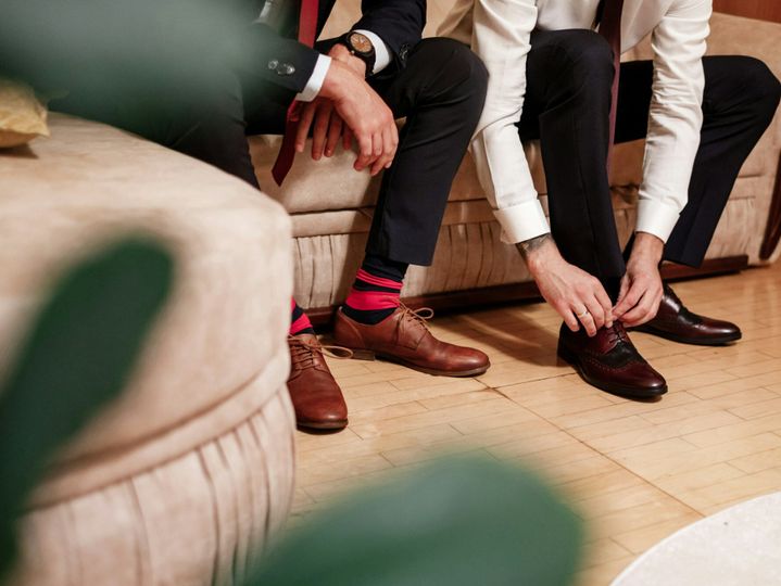 Men's feet in stylish shoes and bright socks. Elegant man dresses shoes. Two men's hands tie