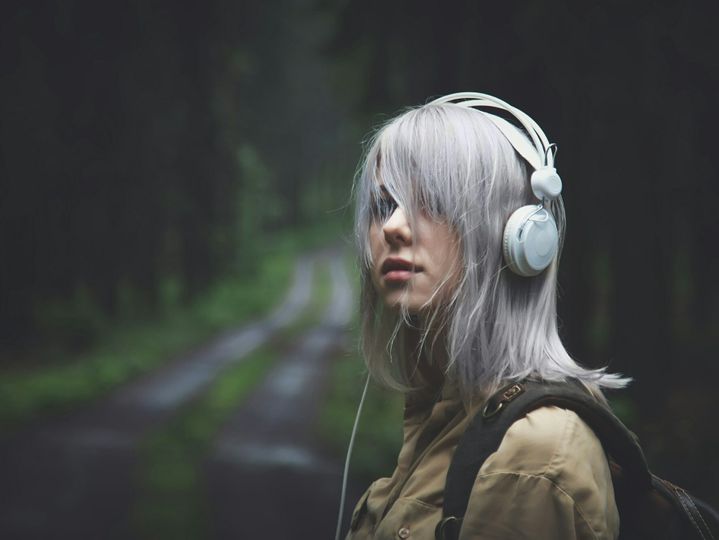 Blonde woman in headphones with backpack in rainy day in forest