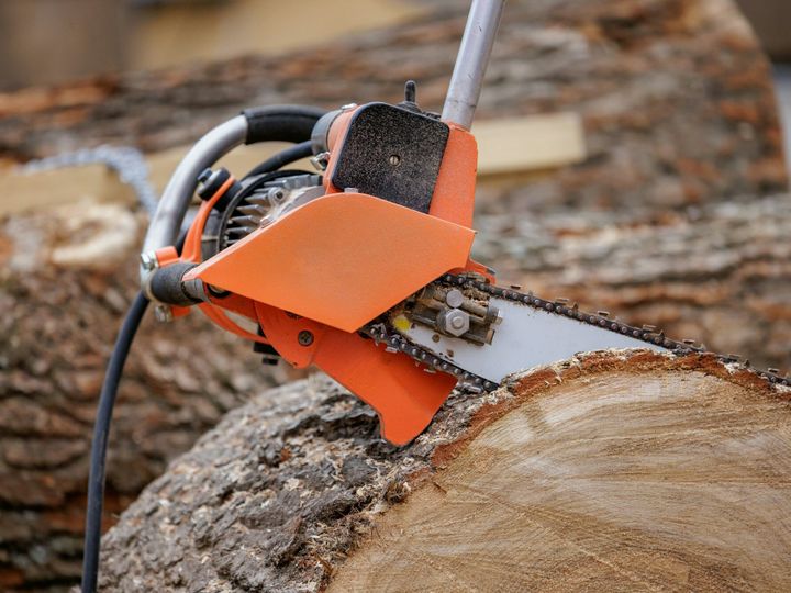 Woodcutter saws tree with electric chain saw on sawmill.