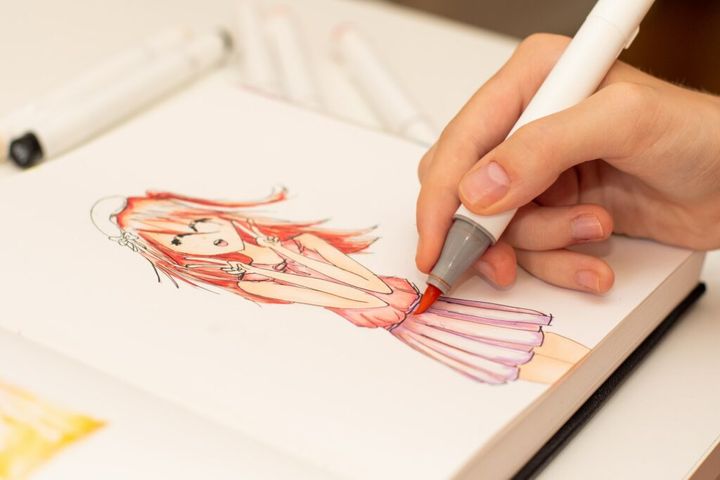 Girl's hand drawing anime manga sketch with alcohol based sketch markers.