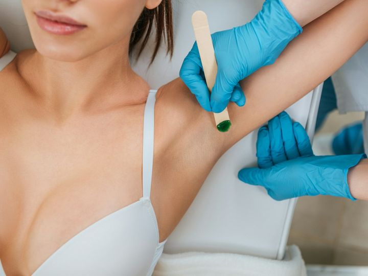 Cropped view of cosmetologist using putty knife for armpit wax depilation