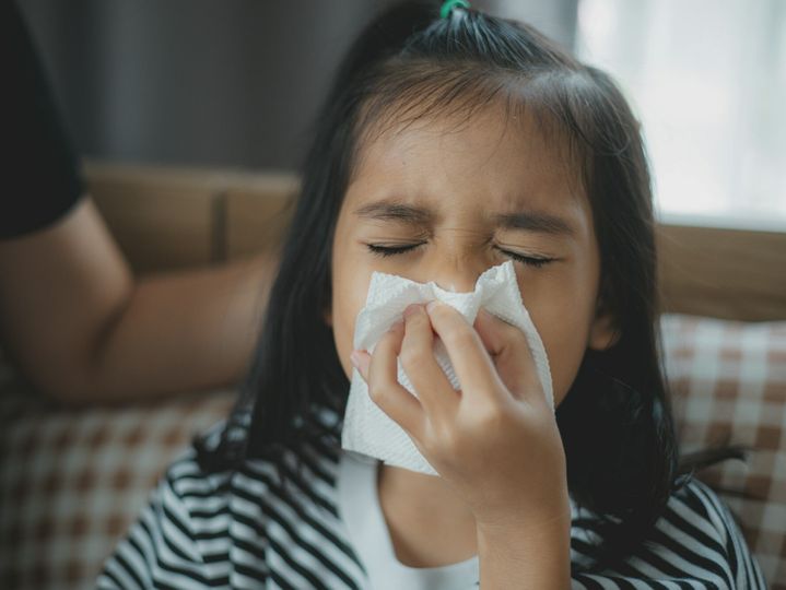 A girl is sniffling and wiping her nose with a tissue