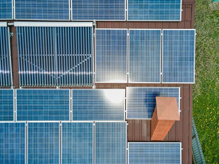 Building roof with rows of blue photovoltaic panels and vacuum air solar collectors