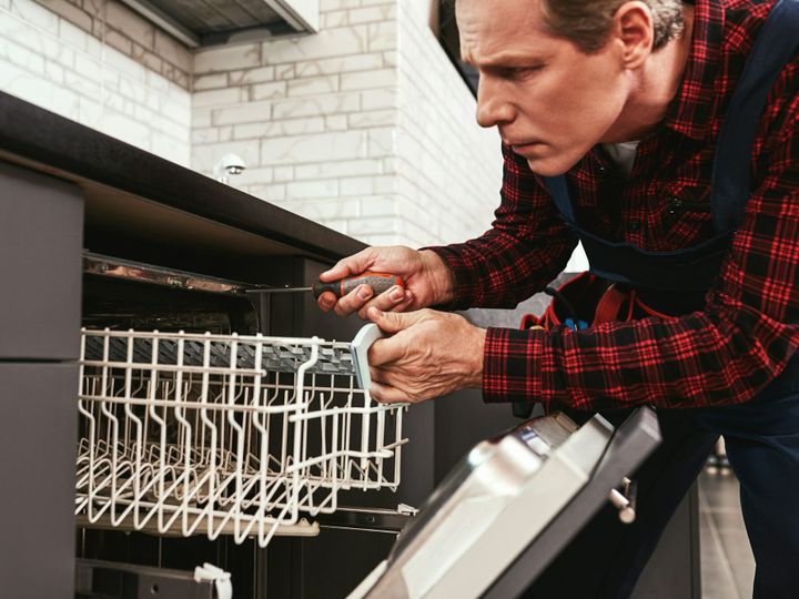 Repairing dishwasher. Male technician sitting near dishwasher