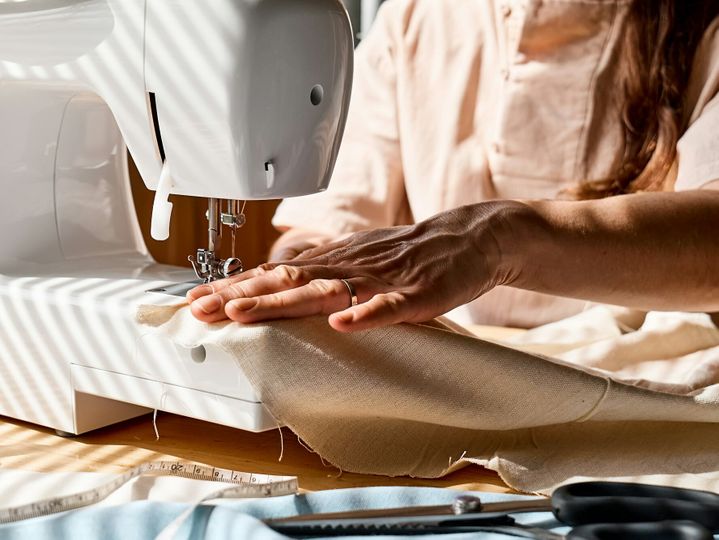 Seamstress sewing linen fabric on sewing machine in small studio.