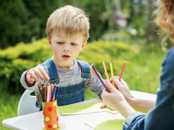 Child selecting colored pencils in garden. Early years. Baby development.