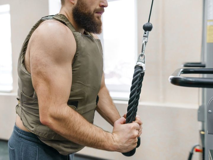 Muscular caucasian bearded man doing exercises dressed in weighted vest in the gym