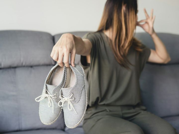 Young woman holding a pair of smelly shoes