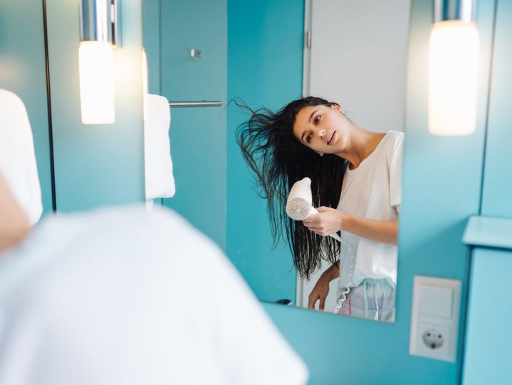 Portrait of young woman using hairdryer in bathroom