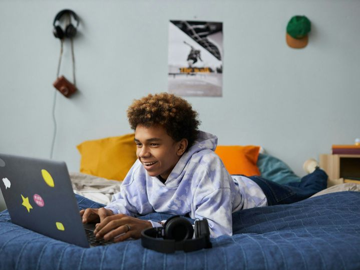 Smiling teenage boy relaxing on bed in front of laptop at leisure