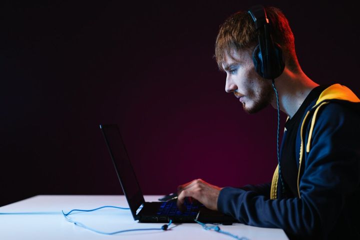Smiling gamer with gaming headsets and laptop in-front on dark background. Mockup