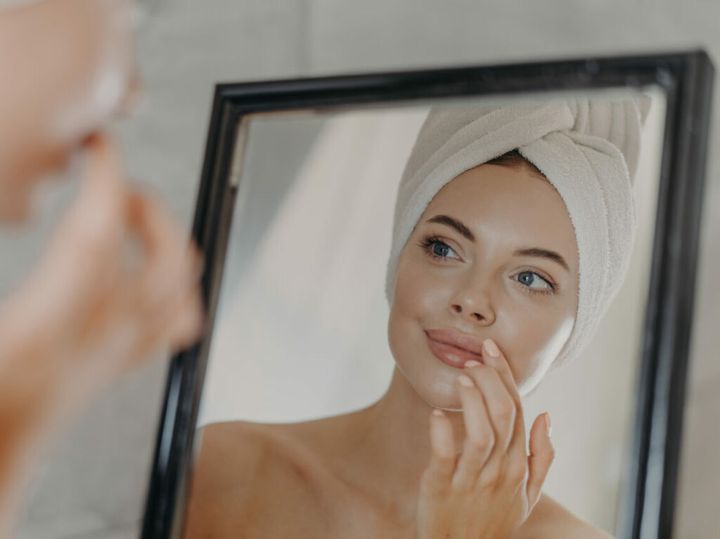 Woman wears minimal makeup, takes care of complexion and lips, looks at herself in mirror