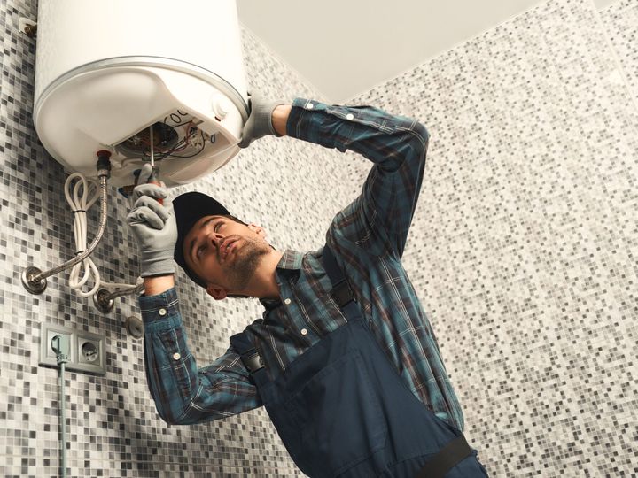 Plumber installing electric heating boiler. Young handyman in uniform setting up electric heating